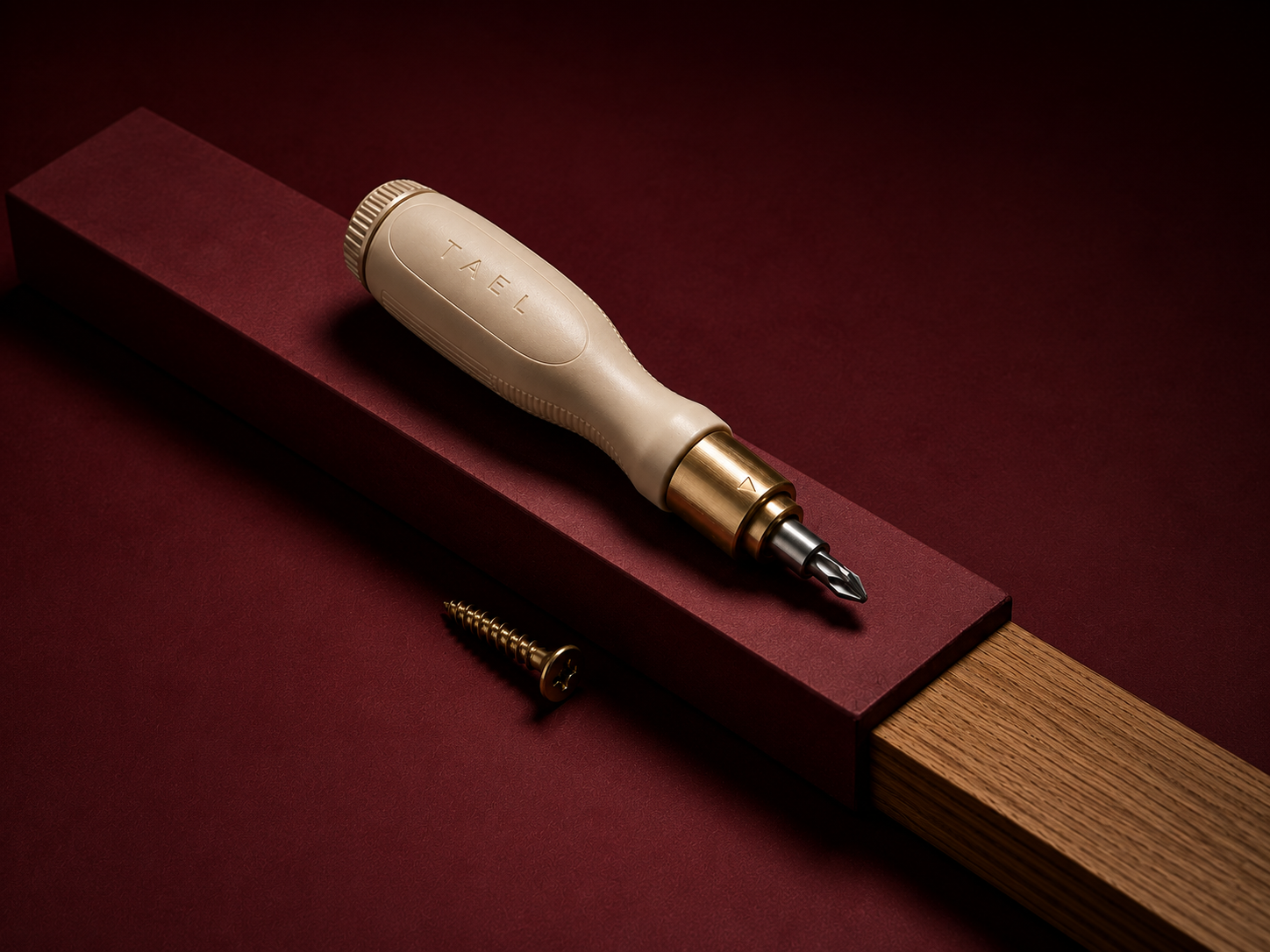 The cream TAEL screwdriver resting on an oxblood plinth beside a brass screw.
